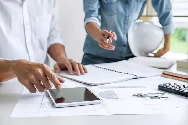 Problemas na gestão de obra: profissionais trabalhando sobre a mesa com projetos de construção civil e utilizando tablet (foto: Adobe Stock)