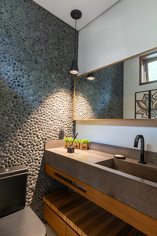 Projeto: Pitta Arquitetura|Lavabo com parede revestida em pedras naturais, que traz textura e um toque rústico sofisticado ao ambiente praiano