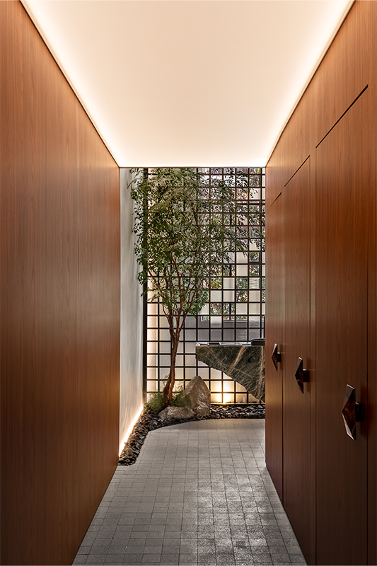 Projeto: Giovanni Vespe |CASACOR São Paulo 2025| Iluminação natural filtrada pelas telas Tensoflex e perfis de LED cria uma atmosfera intimista. A árvore de avencão conduz o olhar, despertando a curiosidade para o espaço escondido ao final do corredor