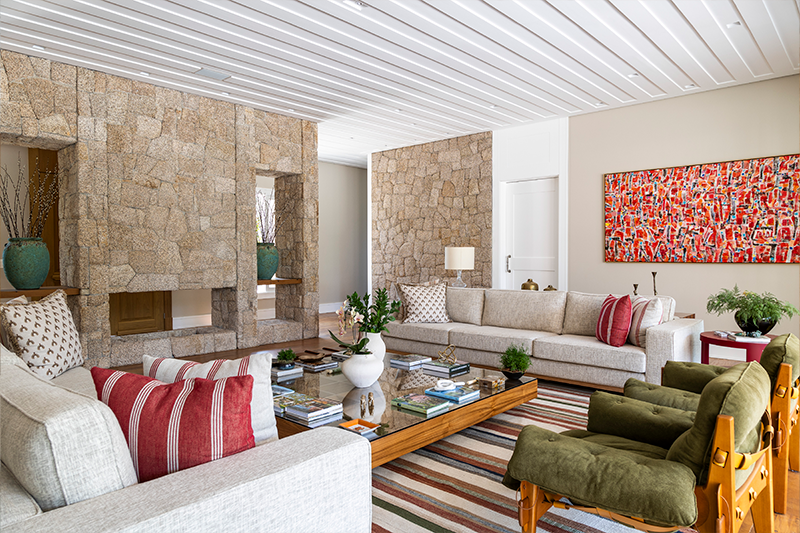 Projeto: Rogério Luciani | Sala de estar marcada pela imponência da pedra natural na parede da lareira, que dialoga com a paleta de cores e texturas.