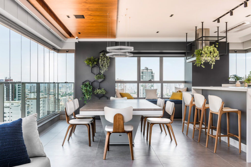 Varanda gourmet com direito a uma vista nas alturas, mesa extensa e bancada em uma cozinha toda equipada com soluções para facilitar a rotina