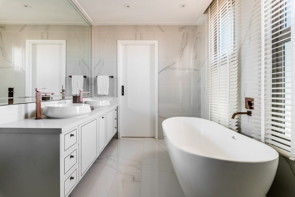 Projeto: Érica Salguero | Banheiro adaptado para casal com banheira, duas pias e armário largo para armazenar