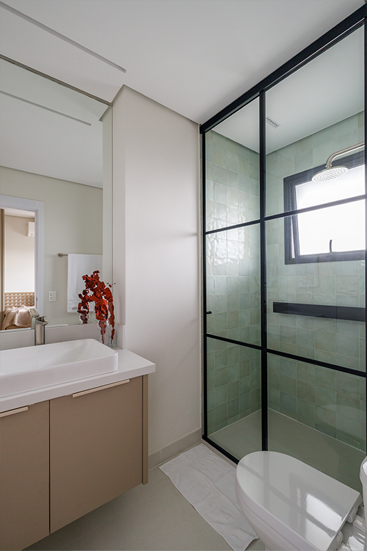 Projeto: Yannick Athia | Banheiros que se complementam: o principal, com duas cubas e cabines separadas; e o segundo, em tons de verde suave, traz leveza e continuidade ao projeto.