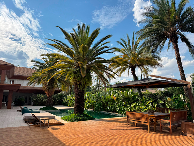 Projeto de arquitetura: Denise Zuba Arquitetos|Ao fundo da piscina há um jardim tropical denso que foi executado especialmente para uma moradora apaixonada por plantas. O verde das espécies contribui para uma paisagem mais natural em meio ao piso de travertino e o deck de madeira.