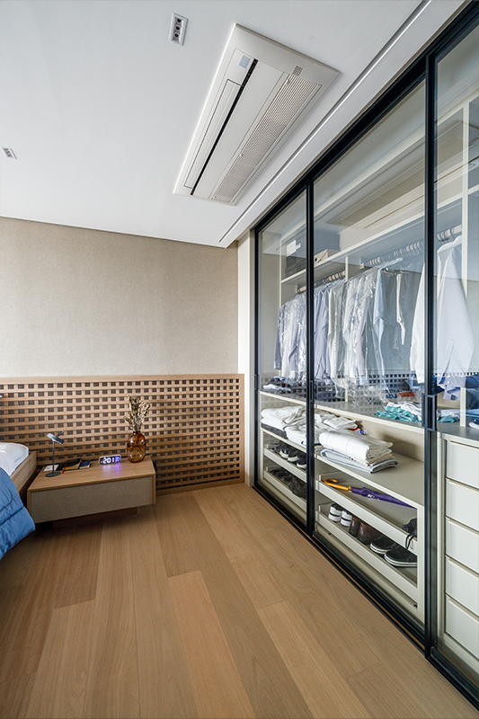 Projeto: Yannick Athia| Suíte ampla e acolhedora, com integração à sacada e cabeceira em muxarabi retroiluminado; cama sob medida, armários com portas de vidro e papel de parede em linho acrescentam textura e serenidade ao ambiente.