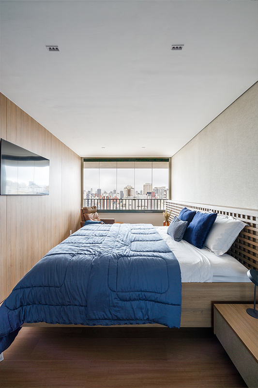 Projeto: Yannick Athia| Suíte ampla e acolhedora, com integração à sacada e cabeceira em muxarabi retroiluminado; cama sob medida, armários com portas de vidro e papel de parede em linho acrescentam textura e serenidade ao ambiente.