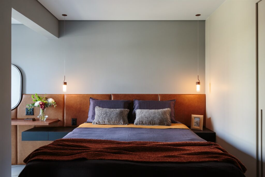 Projeto: Estúdio Maré| Na suíte, o painel em pau ferro integra-se à cabeceira em couro caramelo, criando um clima intimista e elegante..