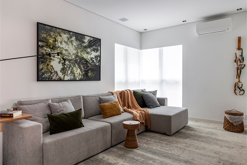 Neste estar com atmosfera de home theater, as paredes brancas e a iluminação natural ampliam e clareiam o espaço. O arquiteto Raphael Wittmann investiu em um sofá modular e retrátil, adornado com almofadas de várias texturas e uma manta drapeada que seguem nuances naturais.