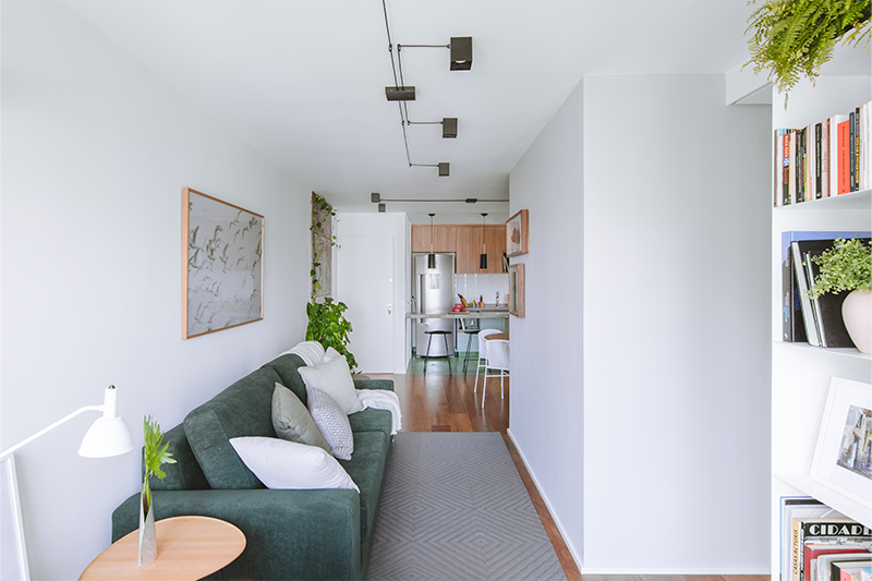 Na reforma deste apartamento antigo, com 70 m², o arquiteto Raphael Wittmann aproveitou a sala de estar, com formato corredor e que dá acesso à área íntima e a varanda, para constituir o layout com sofá, poltrona com apoio para os pés e uma estante onde estão expostos itens decorativos e o acervo de livros dos moradores.