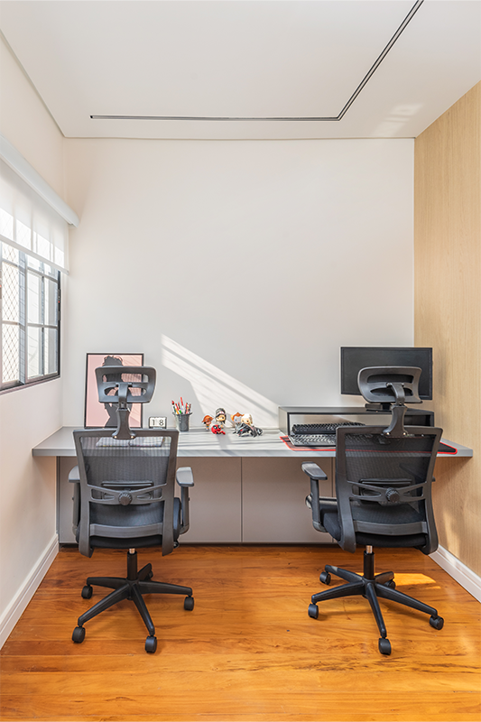 No pavimento superior, o home office compartilhado pelo casal foi posicionado junto à janela, aproveitando ao máximo a iluminação natural. A bancada sob medida melhora o conforto e amplia a sensação de espaço