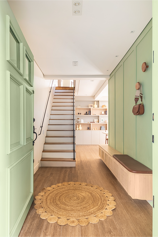 Ao adentrar, o banco suspenso, com 45 cm de distância do piso e fechamento em palhinha, percorre toda a parede lateral. Para o conforto e hábito dos moradores, o interior da marcenaria comporta os sapatos. O arquiteto Bruno Moraes também incluiu penduradores para acomodar bolsas e casacos