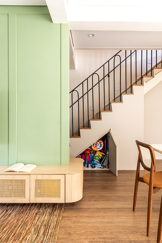 Em zoom nas imagens, a marcenaria curva se repete em todo o projeto. Sob os degraus, além de um armário embutido para organizar os brinquedos da criança, um nicho especial para a caminha do cachorro foi integrado ao cotidiano da casa de forma natural e discreta