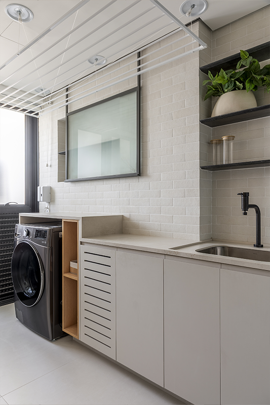 A lavanderia possui uma composição silenciosa de tons neutros, com desenho vertical das superfícies e nichos embutidos na marcenaria para criar ambiente ordenado