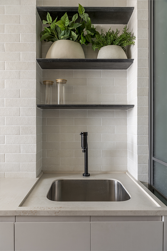 A lavanderia possui uma composição silenciosa de tons neutros, com desenho vertical das superfícies e nichos embutidos na marcenaria para criar ambiente ordenado