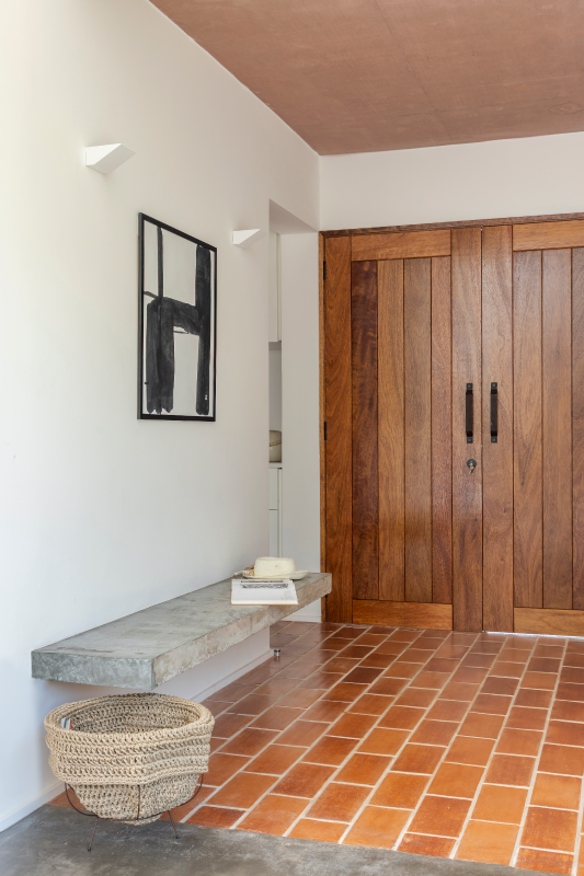 A porta de madeira rústica escolhida pelo arquiteto Raphael Wittmann aquece o conjunto e marca o início de uma jornada arquitetônica que é, ao mesmo tempo, imponente e acolhedora