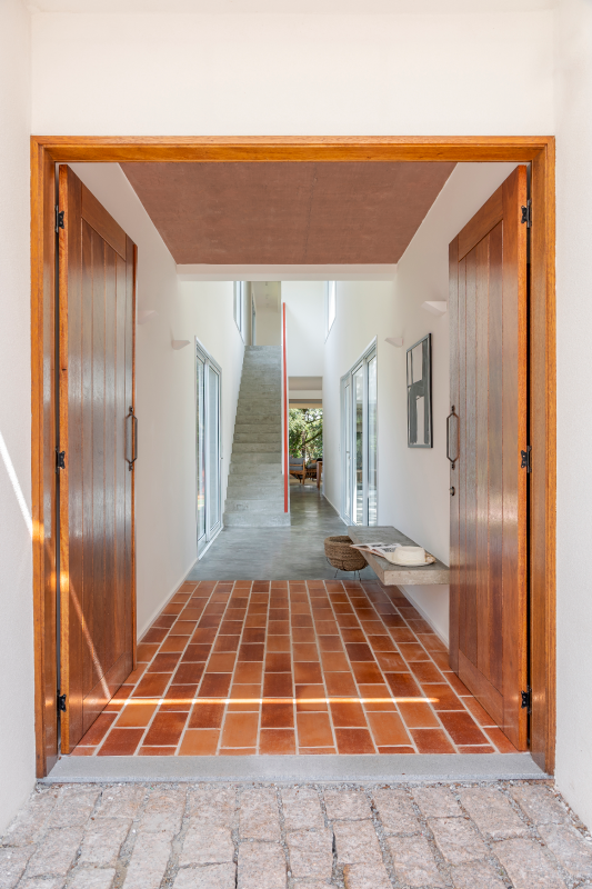 A porta de madeira rústica escolhida pelo arquiteto Raphael Wittmann aquece o conjunto e marca o início de uma jornada arquitetônica que é, ao mesmo tempo, imponente e acolhedora