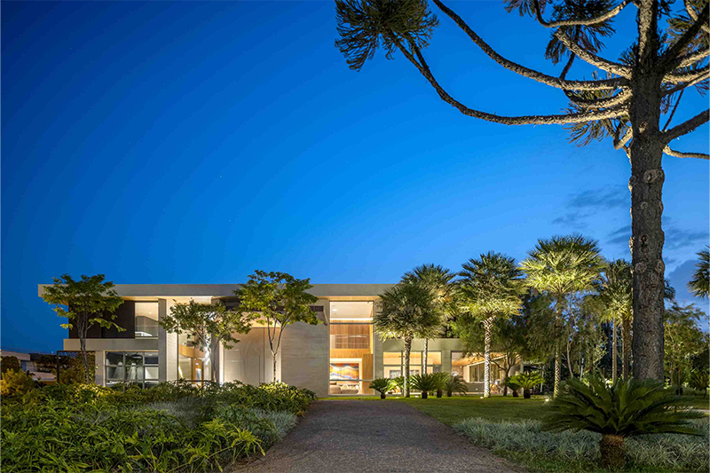 Assim como no espaço de lazer, voltado para o fundo da casa, a área que contempla a frente e as laterais da residência também apresenta variedade de espécies, como carandás e Thaumatophyllum jobim, com um belo jardim e um clima de reconexão com a natureza, que encanta os visitantes logo ao chegar ao local